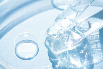 Pipettes with transparent cosmetic liquid or face serum over blue background. Texture of  hydrolate or cosmetic oil, beaty treatments. Selective focus