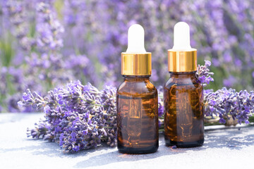 Two dropper bottles with lavender cosmetic oil or face serum against lavender flowers field as...