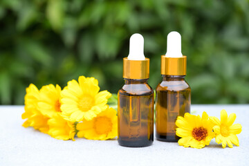 Calendula beauty products. Natural calendula oil in dropper bottles against green leaves as natural background. Herbal cosmetic oil for skincare. Selective focus