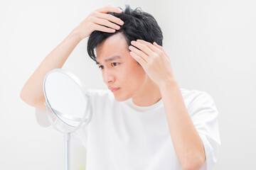 鏡を見て髪の毛を気にする若い日本人男性