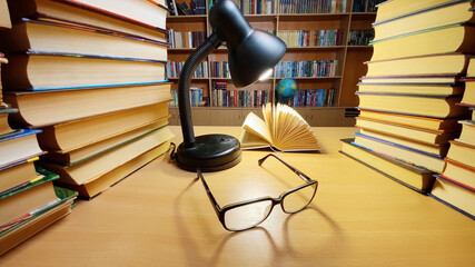 Book on desk in library at lamp and glasses, wind turning pages, bookshelves and globe on background