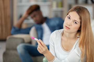 sad young woman holding pregnancy test while sitting on sofa