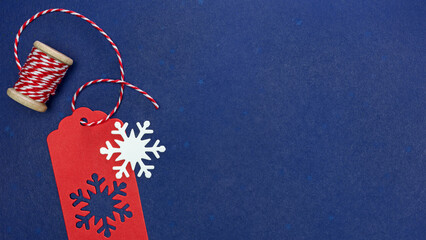 red gift tag with snowflakes and red and white thread on spool. dark blue background. - Powered by Adobe