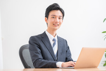 パソコン作業をする若い日本人男性・カメラ目線