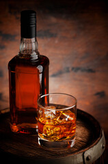 Glass of whiskey with ice cubes and bottle