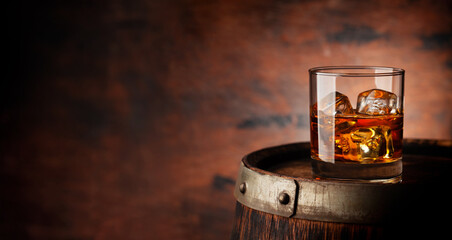 Glass of whiskey with ice cubes on the old barrel