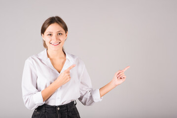 A businesswoman in a white shirt points her fingers at a copy space for advertising on a gray background.