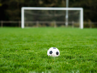 Classic soccer of football ball on the dark green grass field in focus. Goal post out of focus in...