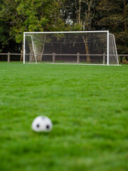 Soccer of football goal posts in focus. Classic ball out of focus in foreground. World wide popular sport activity. Equipment for training.