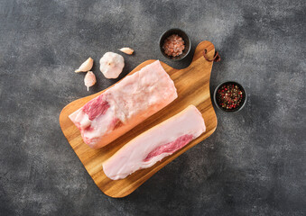 Two pieces of raw pork lard with spices on wooden board, top view