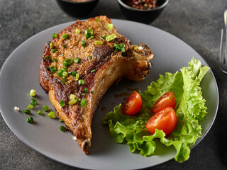 Grilled pork chop on grey plate sprinkled with green onions with salad and cherry tomatoes.