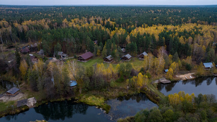 Fototapeta premium panoramic view from a drone on the edge of the forest with wooden houses and a river against the backdrop of autumn nature