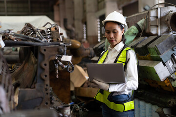 Asian female engineer worker working with laptop computer checking, maintaining machinery, mechanical machine at the industry factory. Asian woman technician wear safety uniform working in the factory