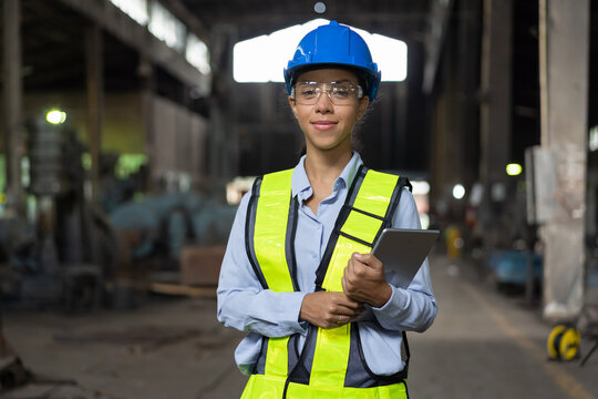 Happy woman engineer worker working with digital tablet at the industry factory area. Female technician wear safety helmet, glasses and uniform checking and working in the factory