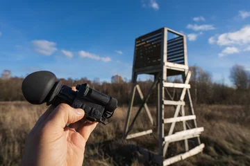  On the hunt, a thermal imaging monocular in hand and a hunting tower in nature. © Dmitri