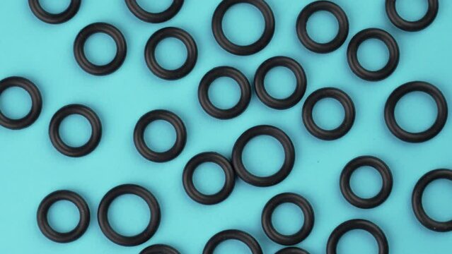 Top view of black elastic rubber sealing gaskets with a round geometric shape on a colored blue background. Rotation. Abstract view