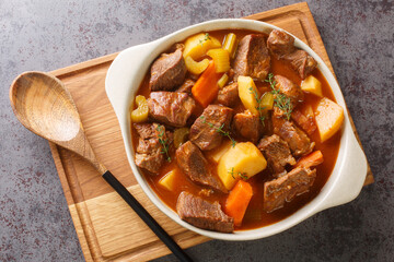 Hearty Irish inspired beef stew made with garlic, stock, Guinness, bacon, potatoes, carrots, and onions closeup in the pot on the table. Horizontal top view from above