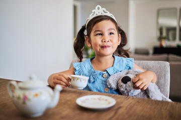 Happiness, tea party and child in her home, playing, having fun with tea set and wearing a crown. Creativity, imagination and young Asian girl enjoying toys, teddy bear and toy kitchen utensils - Powered by Adobe