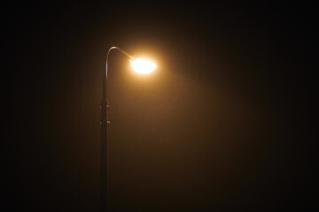 One night lamppost shines with faint mysterious yellow light through evening fog. Streetlight shine at quiet city night, magic atmospheric light in mystical darkness, copy space