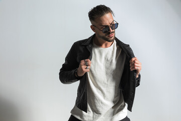 Fototapeta premium cool man with stylish wet hair pulling and adjusting black leather jacket