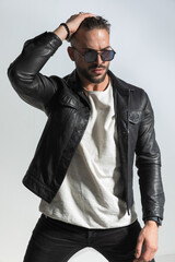 arrogant man in black leather jacket looking away while adjusting hair