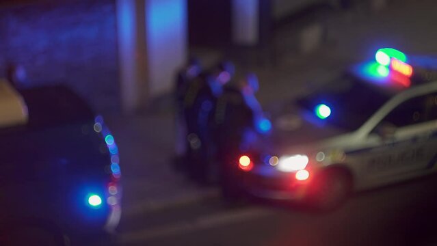 Group of police officers around blinking cop car, beacon light, blurry night view