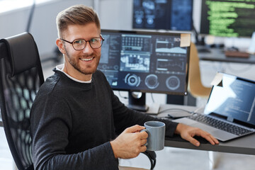 Portrait of young software engineer smiling at camera while posing at workplace in office with...