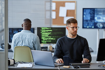 Portrait of young Caucasian man using computer while programming software in office, copy space