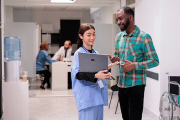 Young man scheduling new appointment with asian doctor at health care institute. Sanatorium staff attending african american patients. Nurse aide displaying tests on computer.