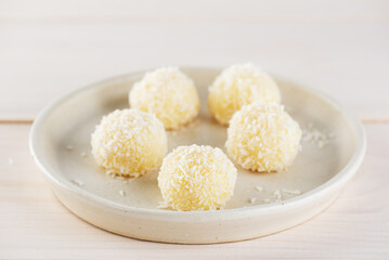 Candy truffles brigadeiro with coconut on a plate on a wooden table.