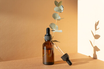 Unmarked glass bottle with dropper lid with drop of serum on brown background. Cosmetic container...