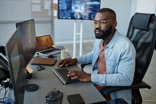 Portrait of black game developer working on level design and using computer in office