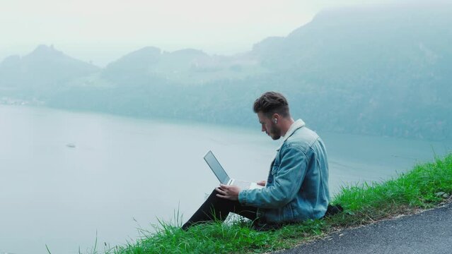 Handsome man typing on notebook computer keyboard. Man work out of office on epic nature landscape, feeling excitement, getting good news, feeling euphoria, raising arms. Feel of success, victory, joy