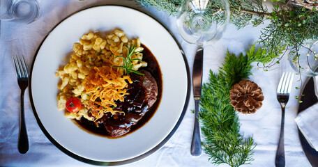 Rinderfilet Steak mit Spätzle zu Weihnachten an einem festlich gedeckten Tisch mit Tannenzapfen...