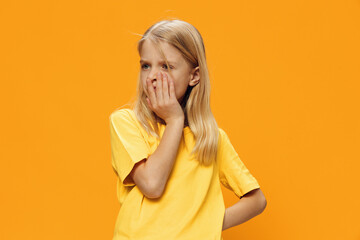 a cute, thoughtful girl stands on a yellow background in a yellow T-shirt with a very puzzled face....