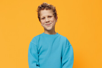 portrait of a cute, pleasant boy with curly hair in a blue sweater on a yellow background,...