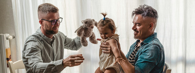 Horizontal banner or header with male gay couple with adopted baby girl at home - Two handsome fathers playing with their daughter - Lgbtq family at home - Diversity concept LGBTQ family relationship - obrazy, fototapety, plakaty