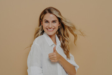 Excited beautiful blonde female posing in studio with thumb up ok sign