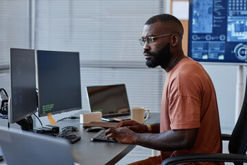 Side view of black software engineer using computer in high technology office, data systems and...