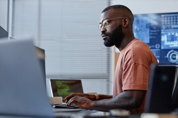 Side view portrait of black software developer using computer in high technology office, data systems and programming - obrazy, fototapety, plakaty