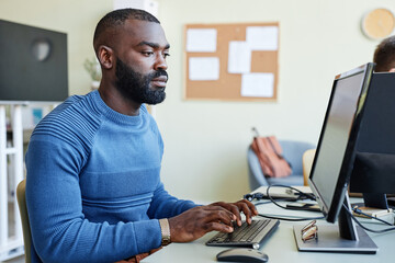 Fototapeta na wymiar Side view portrait of bearded black man using laptop in office while programming software