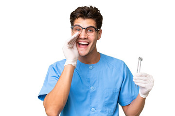 Young dentist man holding tools over isolated background shouting with mouth wide open