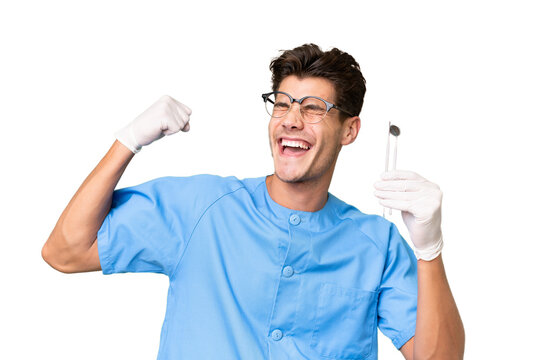 Young dentist man holding tools over isolated background celebrating a victory