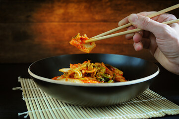 Hand holding kimchi in a chopsticks. Traditional Korean cabbage in a bowl