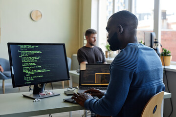Side view portrait of black software engineer writing code at workplace in office with multiple devices