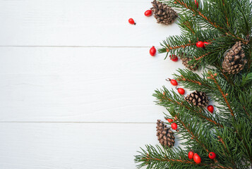 Spruce, fir branches, cones, red berries on white wooden background. Frame border. Christmas New Year composition background. Space for text.