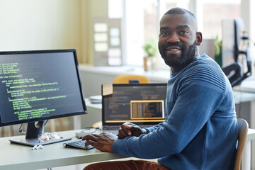 Portrait of black man as computer programmer looking at camera while writing code at office workplace