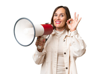Middle-aged caucasian woman over isolated background holding a megaphone and showing ok sign with...