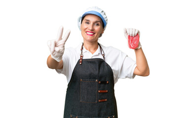 Butcher woman wearing an apron and serving fresh cut meat over isolated background smiling and showing victory sign