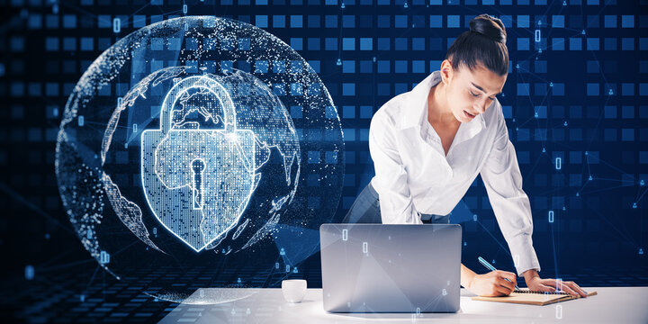 Attractive Young European Businesswoman Leaning On Desktop With Laptop And Writing With Abstract Glowing Padlock And Globe Hologram On Blurry Blue Background. Global Web Safety And Protection Concept.